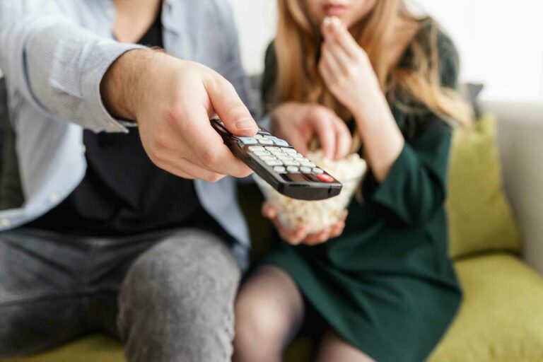 mennesker der sidder i sofaen med fjernbetjeningen
