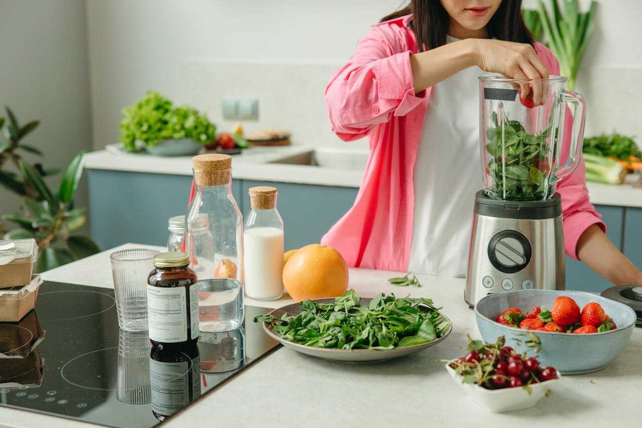 Kvinde i køkken der laver en sund smoothie med sin blender